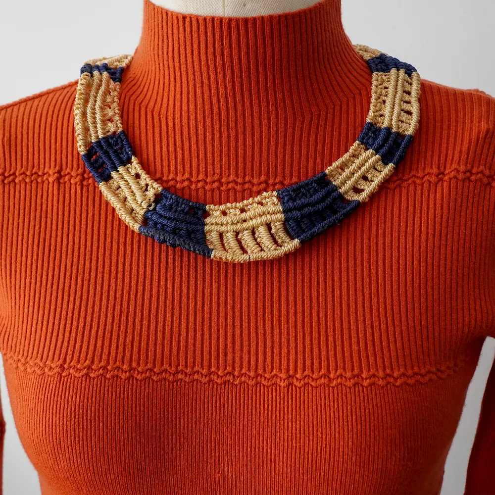 Collar de macrame en colores metalicos sobre maniqui con traje anaranjado