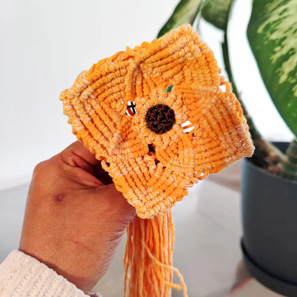 Manos de mujer mostrando flor hecha de macrame