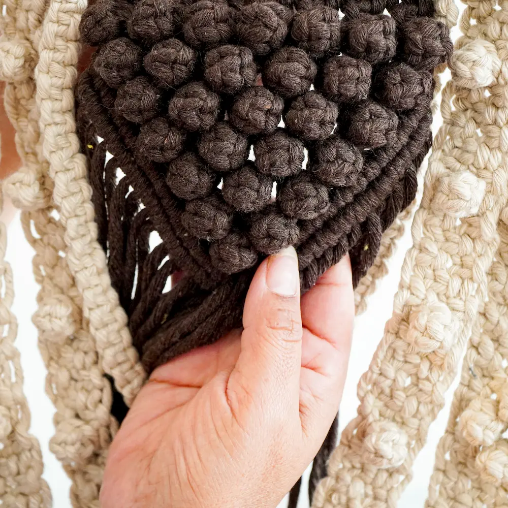 Manos mostrando nudo macadamia de macrame en color marrón