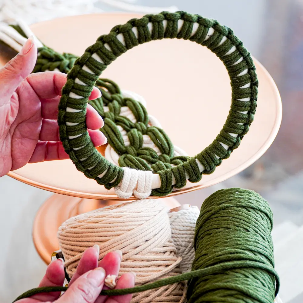 Manosmostrando un aro envueolto con nudo de macrame en color verde